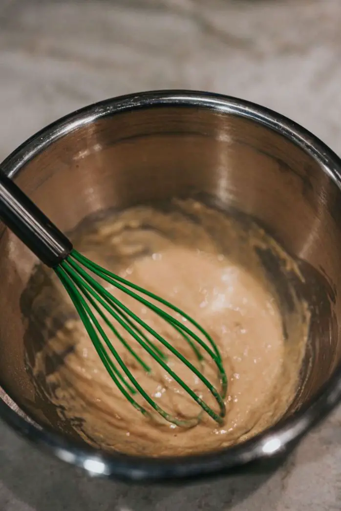 A Cake batter in a steel pan with a whisk
