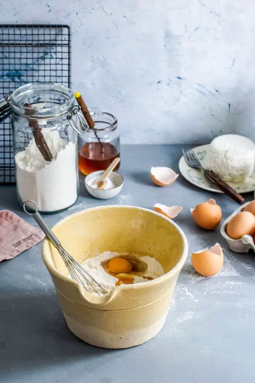 brown mixing bowl with eggs and-flour with whisk