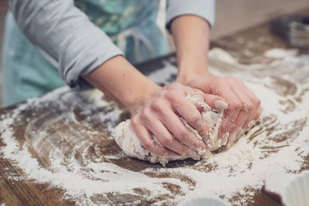A standing person is kneading the dough with hands