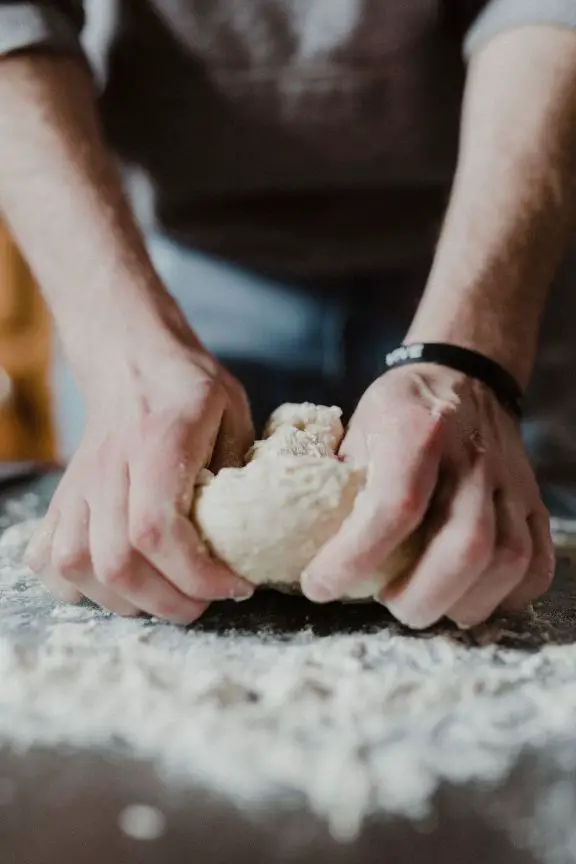 A Person holding white dough on wooden table - what does bread dough enhancer do