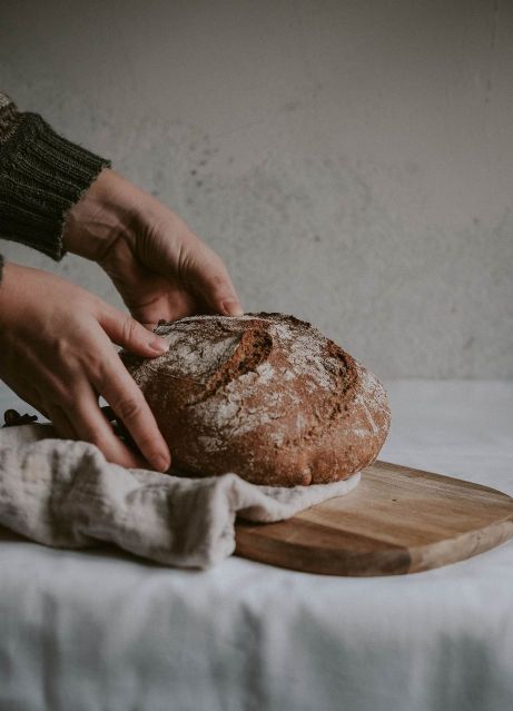 A person holding sourdough bread on brown wooden chopping board